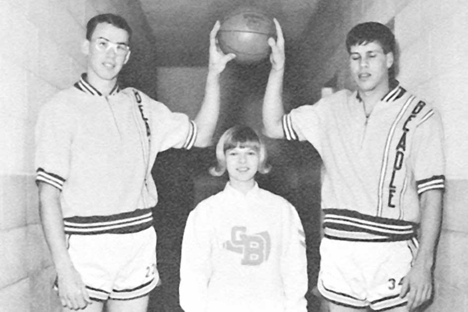 Two players on the 1966-67 basketball team tower over one of the cheerleaders.