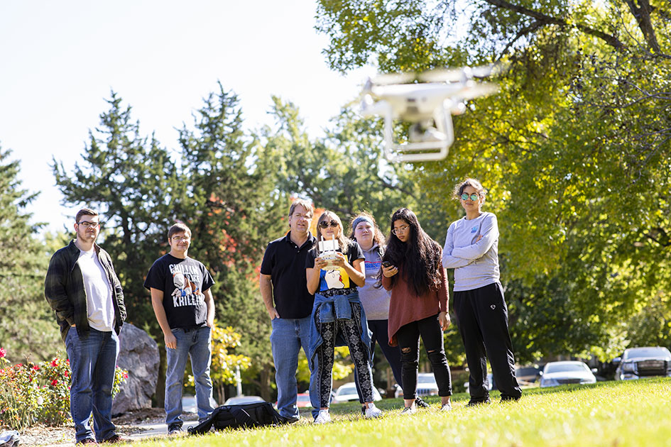 students outside in field flying a drone with a professor for class