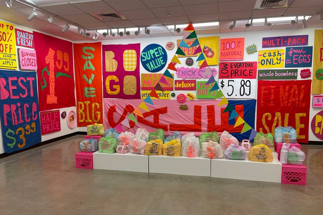 Noelle Vainikka art exhibition impulse featuring bright signage of pricing and advertisements with bags of garbage displayed in the middle of the floor.