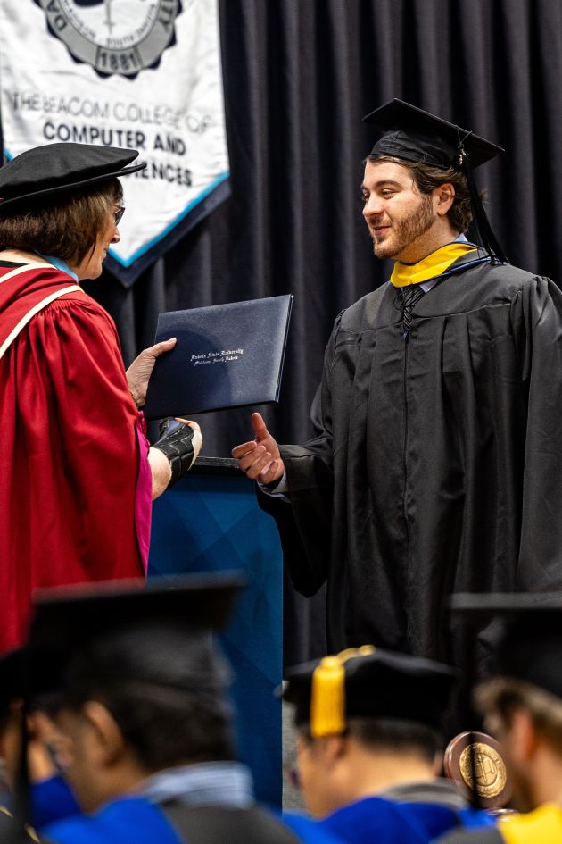 DSU Master's student walking across the stage at commencement recieving their diploma