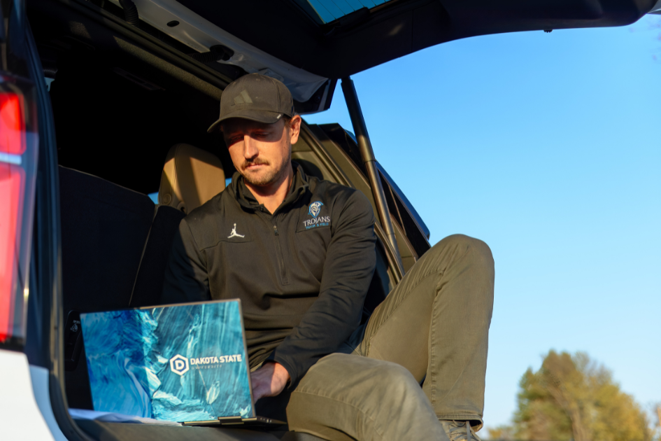 Online student studying in trunk of car on computer