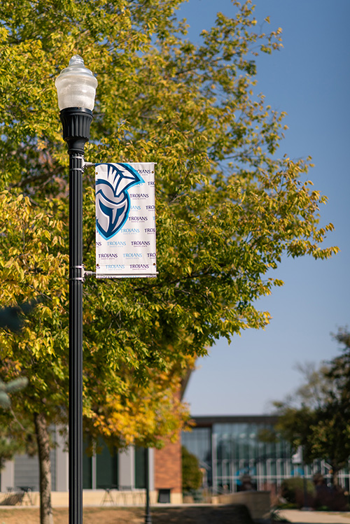 A Dakota State University sign hangs from a lamp post in front of autumn leaves.