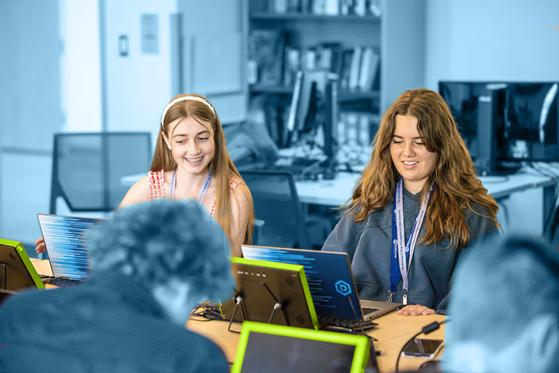 Two gencyber students smiling while working on computer