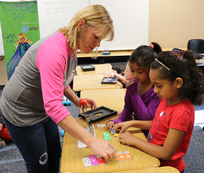 CybHER co-founder Pam Rowland helps two elementary students