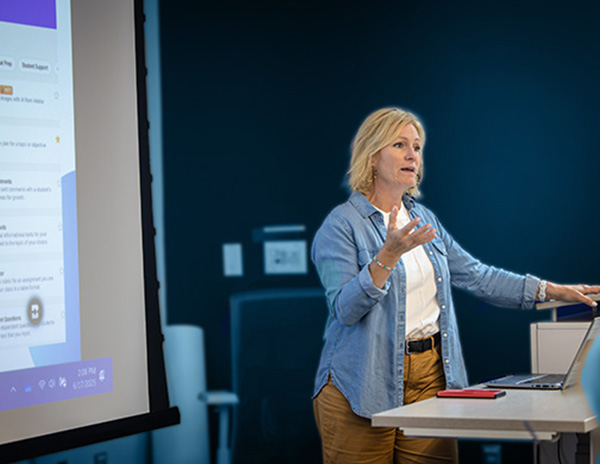 An instructor lecturing a class of campers in front of a projection of a computer desktop.