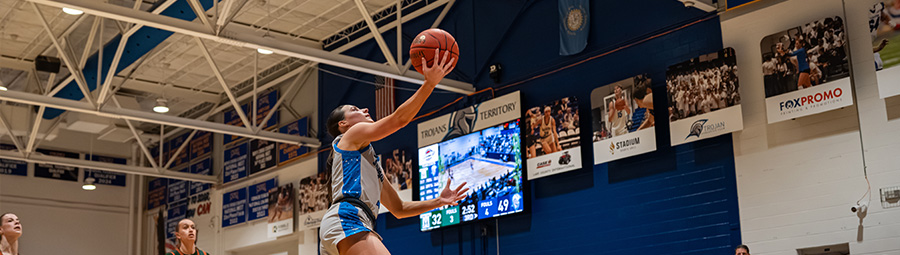 A trojan basketball player jumps into the air with the ball outstretched in her hand