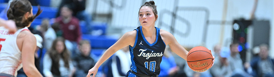 Women's trojans basketball player holding a ball in an outstretched hand as she faces an opponent.