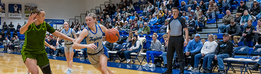 A women's trojan basketball player dodges an opponent in a crowded arena while dribbling the ball.