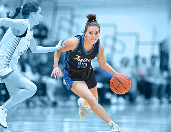 A player in a Trojan's basketball jersey dribbles a ball while avoiding an opponent.