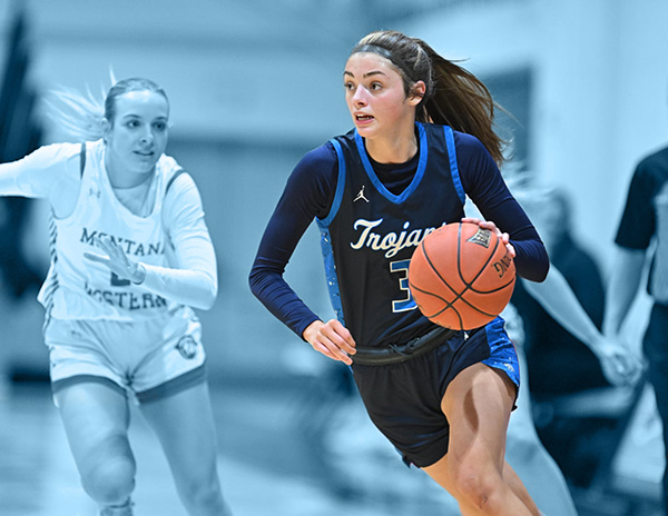 A young woman sprinting while dribbling a basketball evades an opponent.