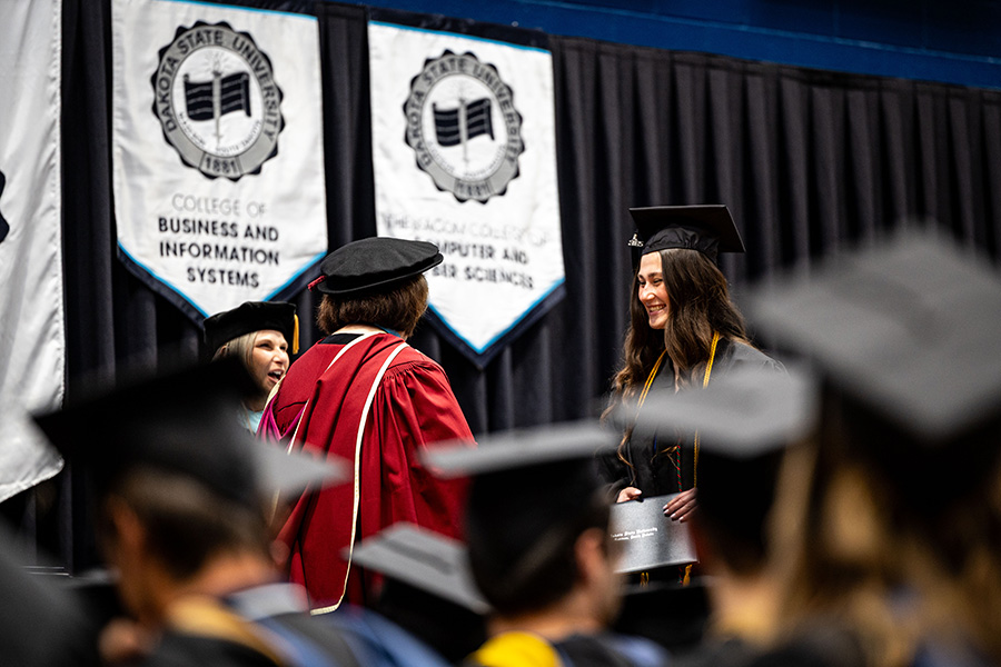 A dakota state university graduate crosses the stage to shake hands with the president during commencement.