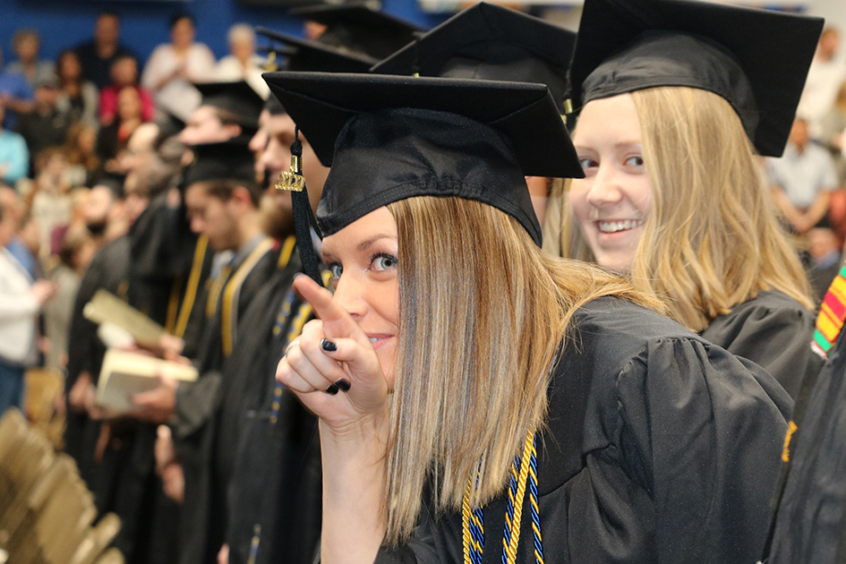 Dakota State University graduate during commencement, pointing to family in the audience