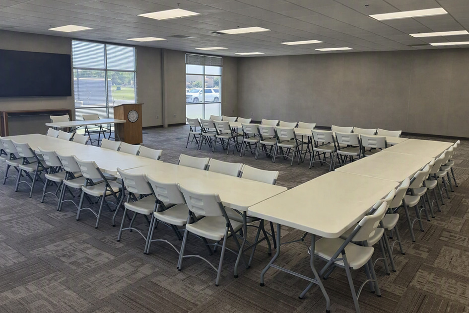 An open conference space with rectangualr tables with folding chairs set up in a U shape. A podium bearing DSU's crest sits at the open side of the U.