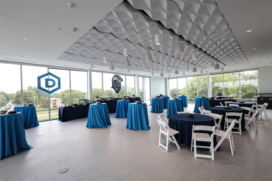 The Heartland captains club is a bright space with floor to ceiling windows on three of the four walls and a textured white ceiling. There is a mix of high and low round tables, the latter of which are surrounded by tasteful wooden white chairs.