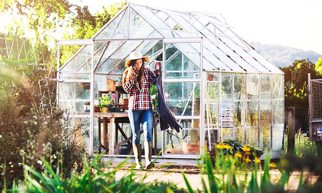 Girl with gardening gloves and hat working outside a greenhouse
