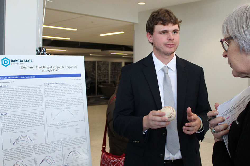 Sammy Drummond, physical science major, explains his research project poster 