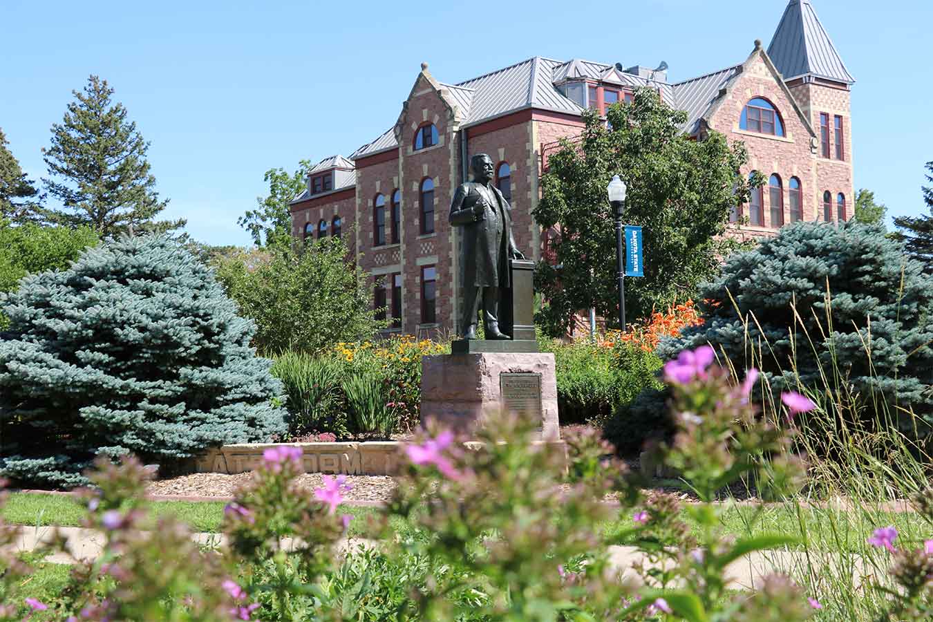 Summer campus photo featuring flowers, a statue of General Beadle, and Beadle Hall