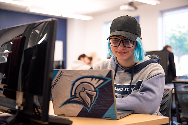 Application development student with blue hair smiling at laptop.