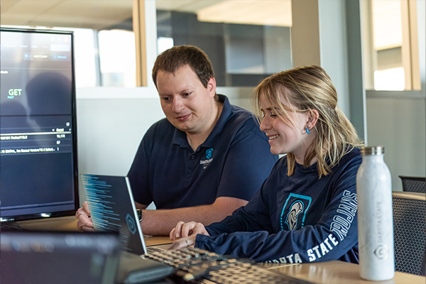 Cyber operations doctoral student sitting with a professor at a laptop.