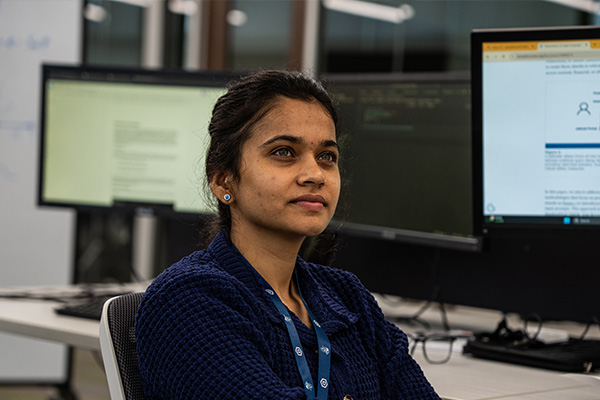 Student sitting with computer monitors behind her.