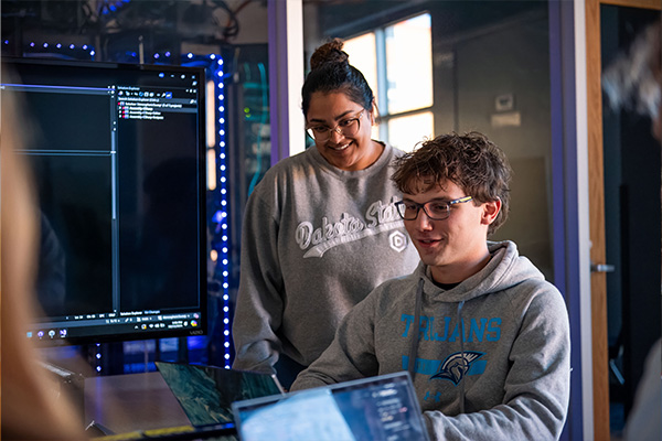 two people looking at a computer with rows of lights and servers behind them