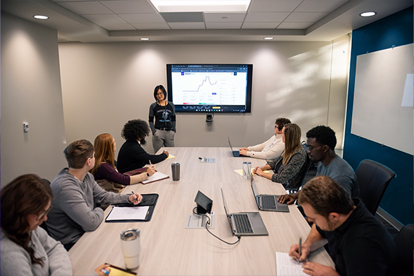 Business Finance professor giving a presentation to a group of finance students in a conference room