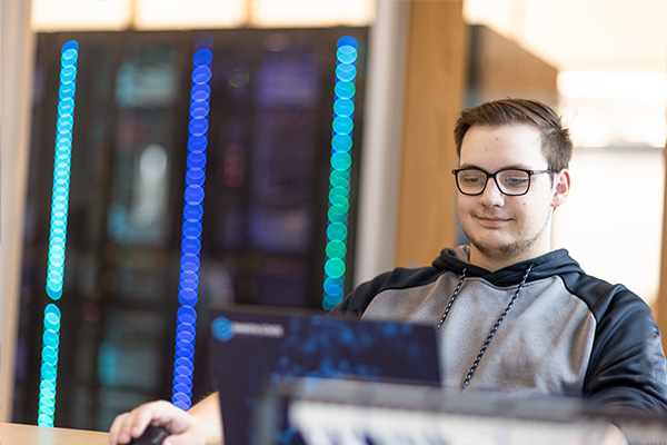 Computer education student working on laptop in front of a server.