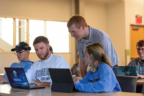 Computer science students looking at a computer with a professor.