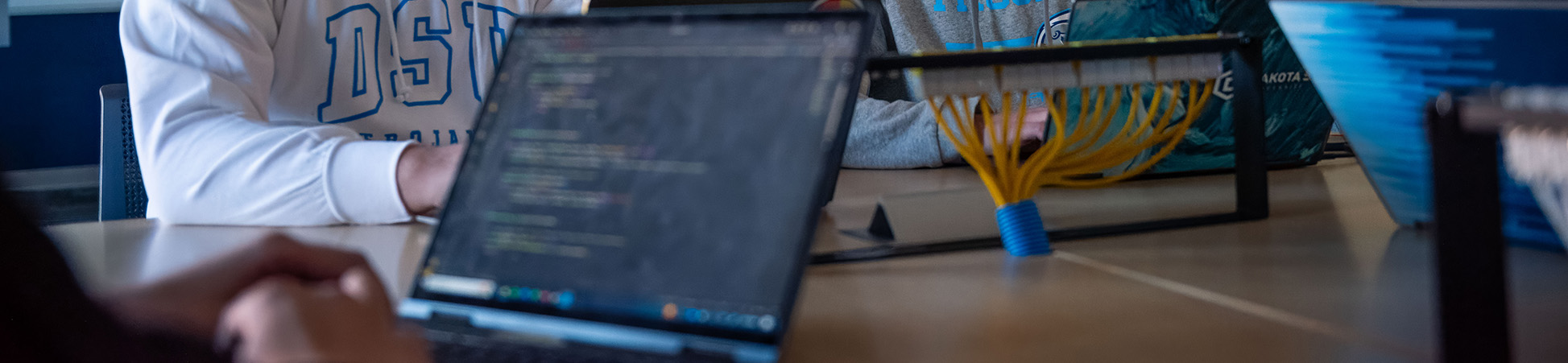 A closeup of laptops with code and a desk with yellow network cables extending out of it.