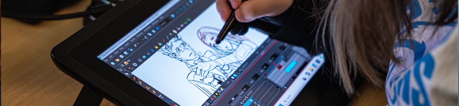 Animation student works with a stylus on a digital drawing tablet filling out details on a sketch of two animated characters. 