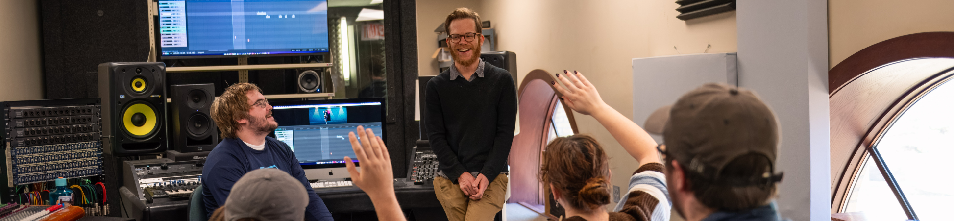 Two sound design students working in a recording studio with audio software displayed on their computer screen.