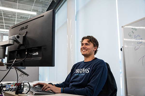 Financial technology student working at his computer with a big grin on his face. 