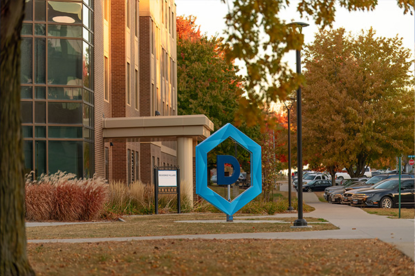 large blue DSU Hex logo sign on campus in autumn