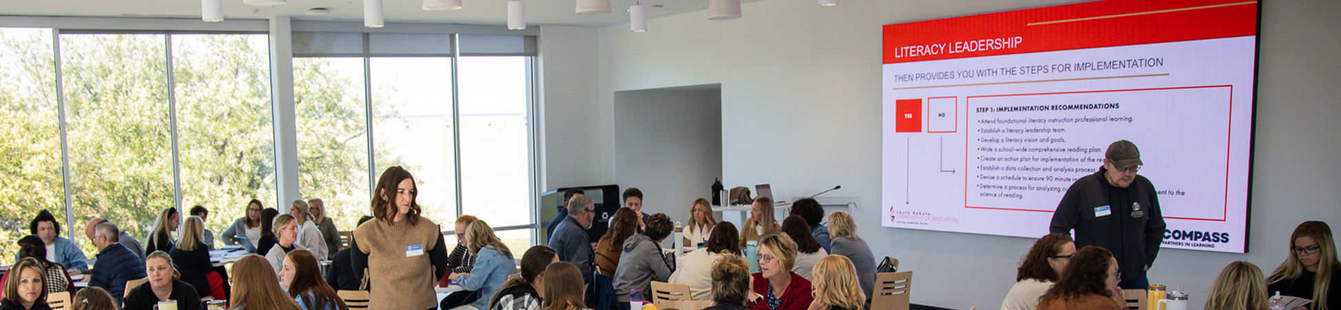 Educators attending a lecture with a presentation slide on the screen titled Literacy Leadership.