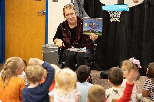 A teacher holding a children's book up to a group of attentive children.