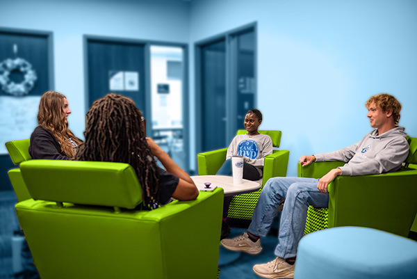 Four students sitting in a circle on chairs, having conversations.