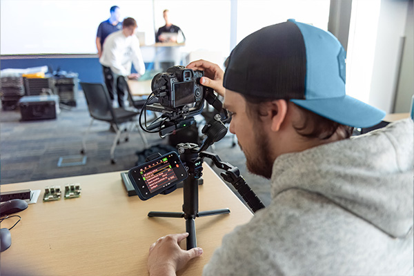 Video production student working with a camera rig that has a cellphone attached displaying technical information.