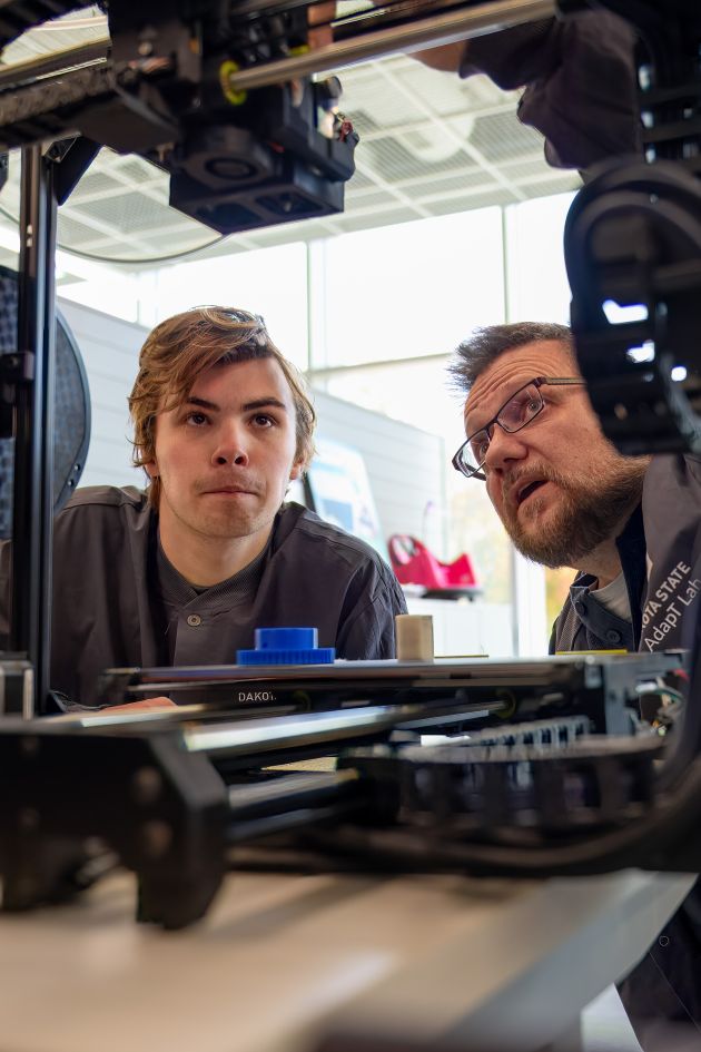 Student and professor looking working on a machine in MadLabs building