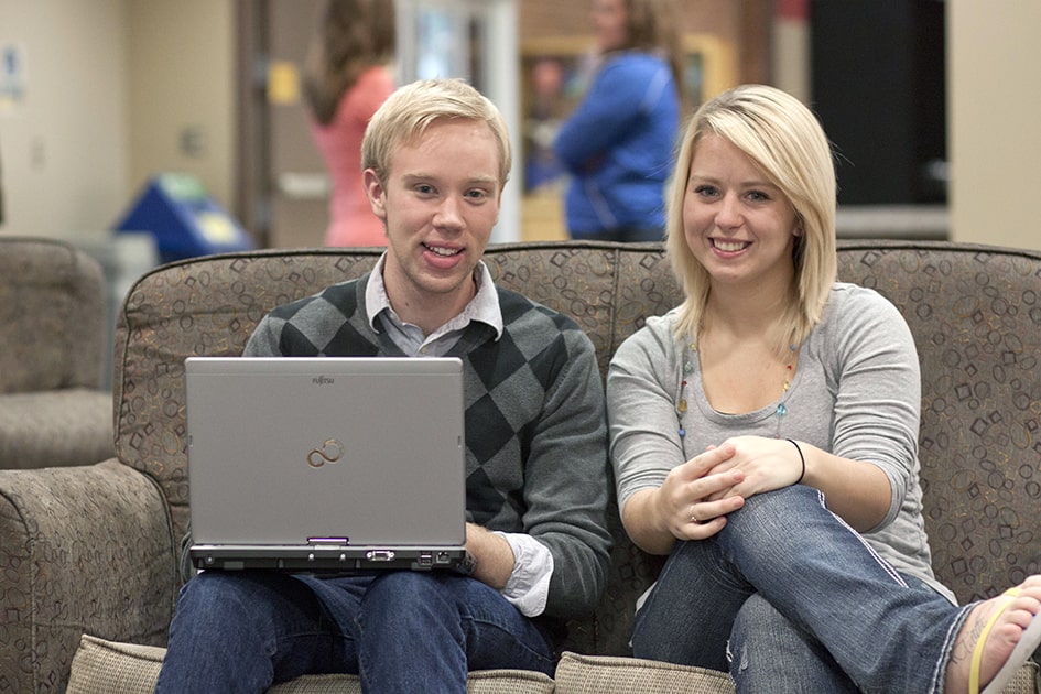 two people sitting on couch looking at laptop
